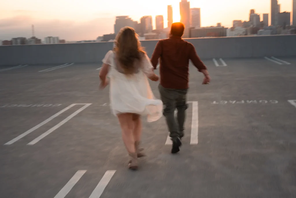 Recently enageged couple running towards sunset on rooftop